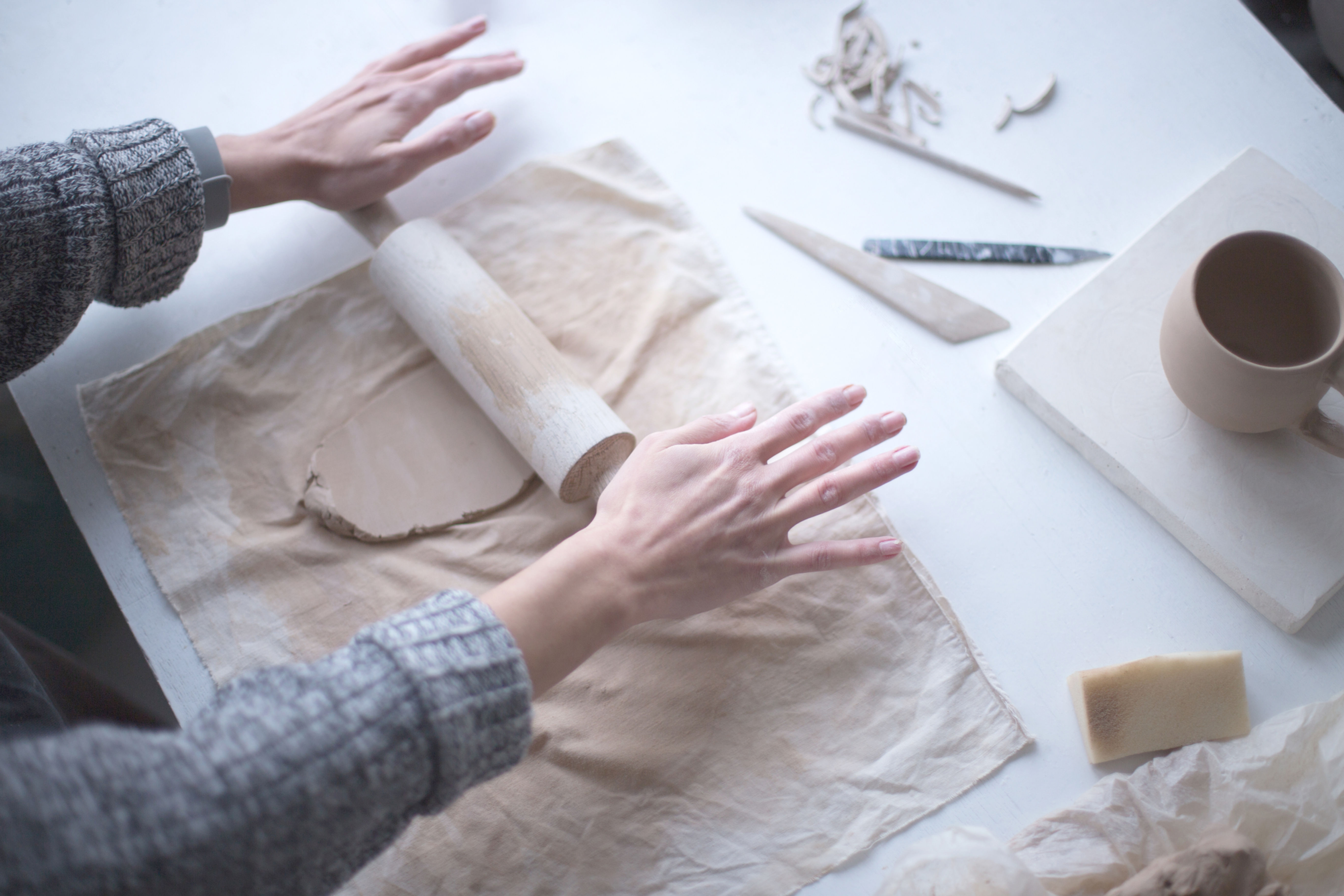 Hands rolling and shaping clay on pottery work surface