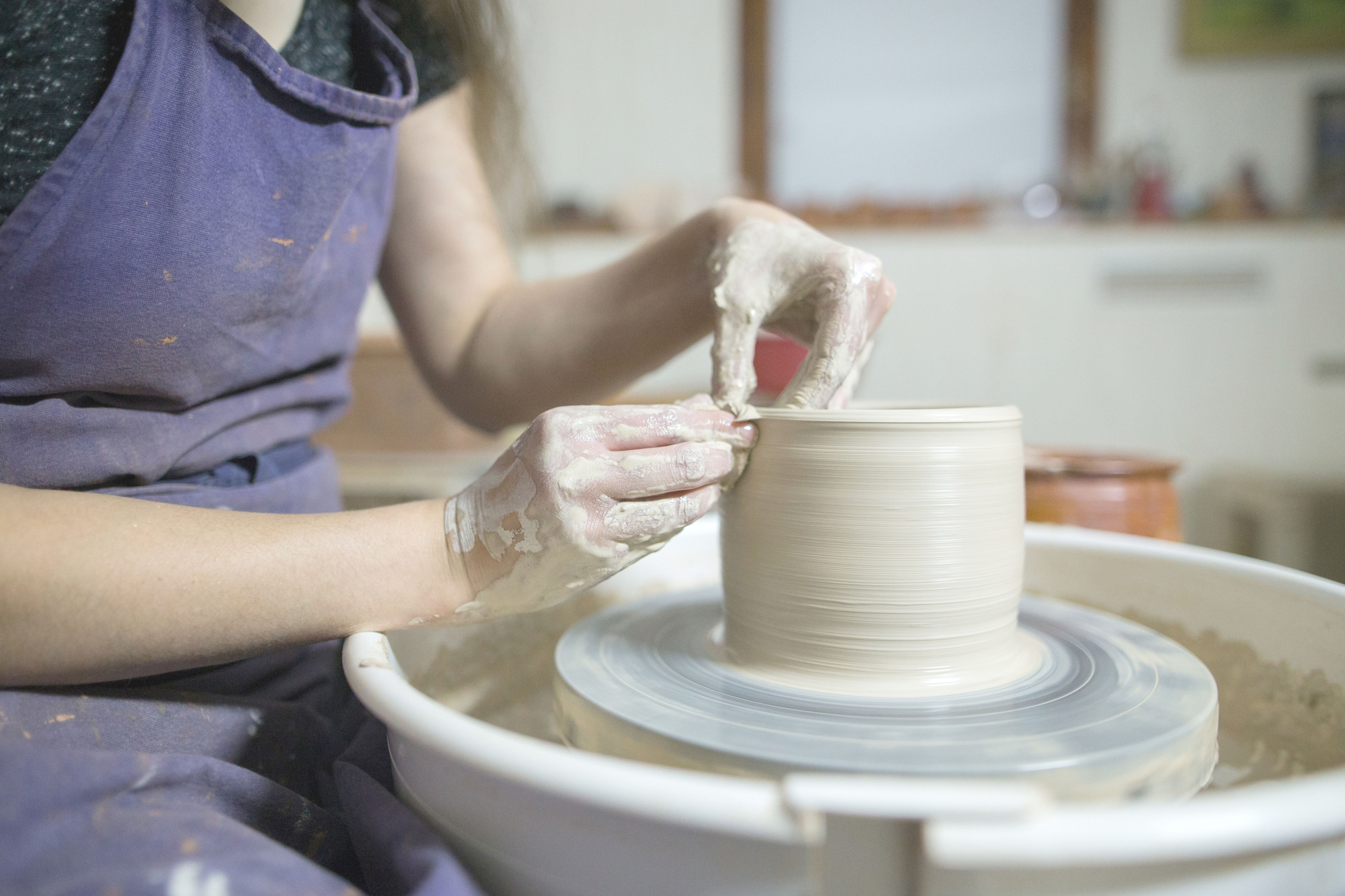 Potter's wheel with hands shaping a mug from clay